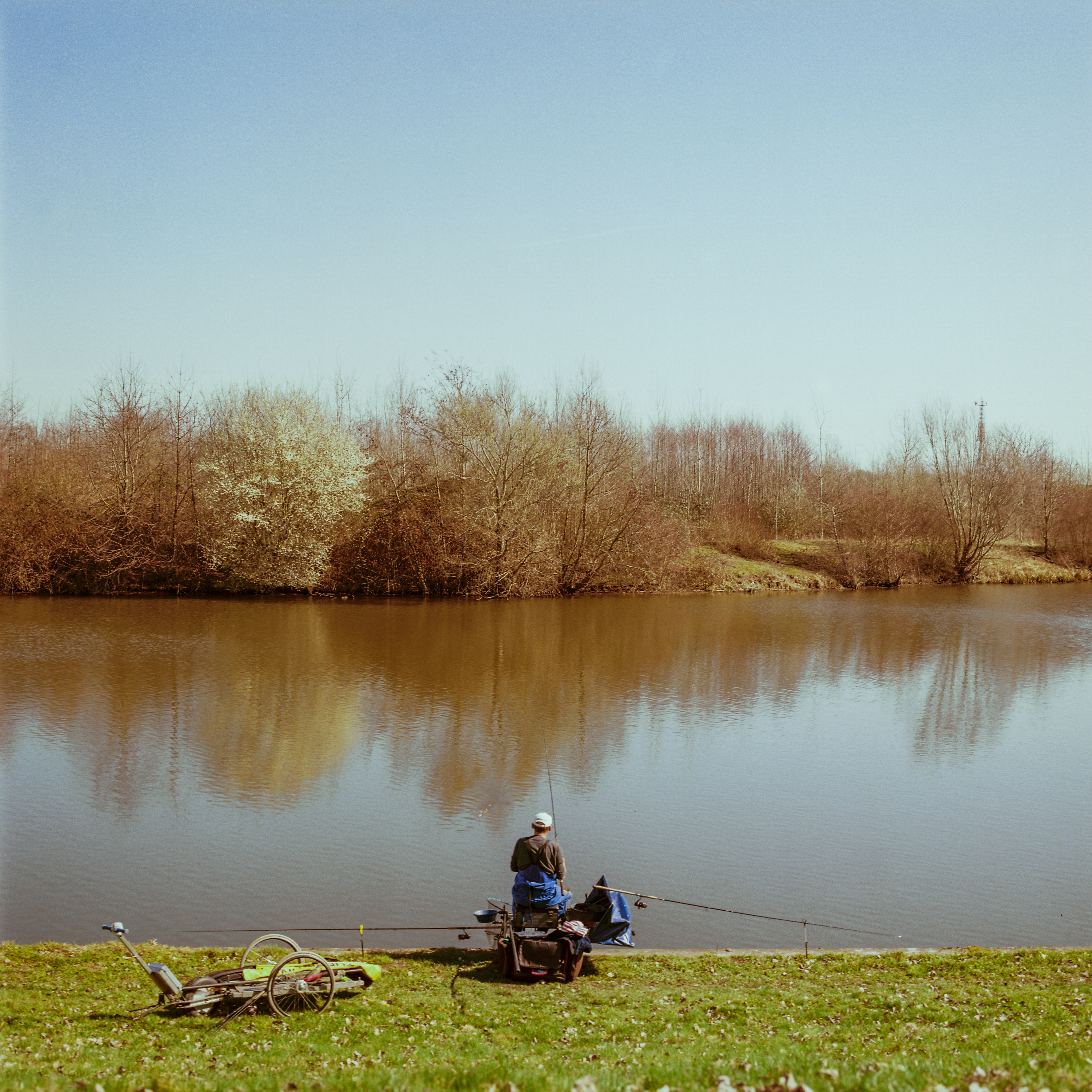 man in red jacket sitting on brown wooden bench near lake during daytime